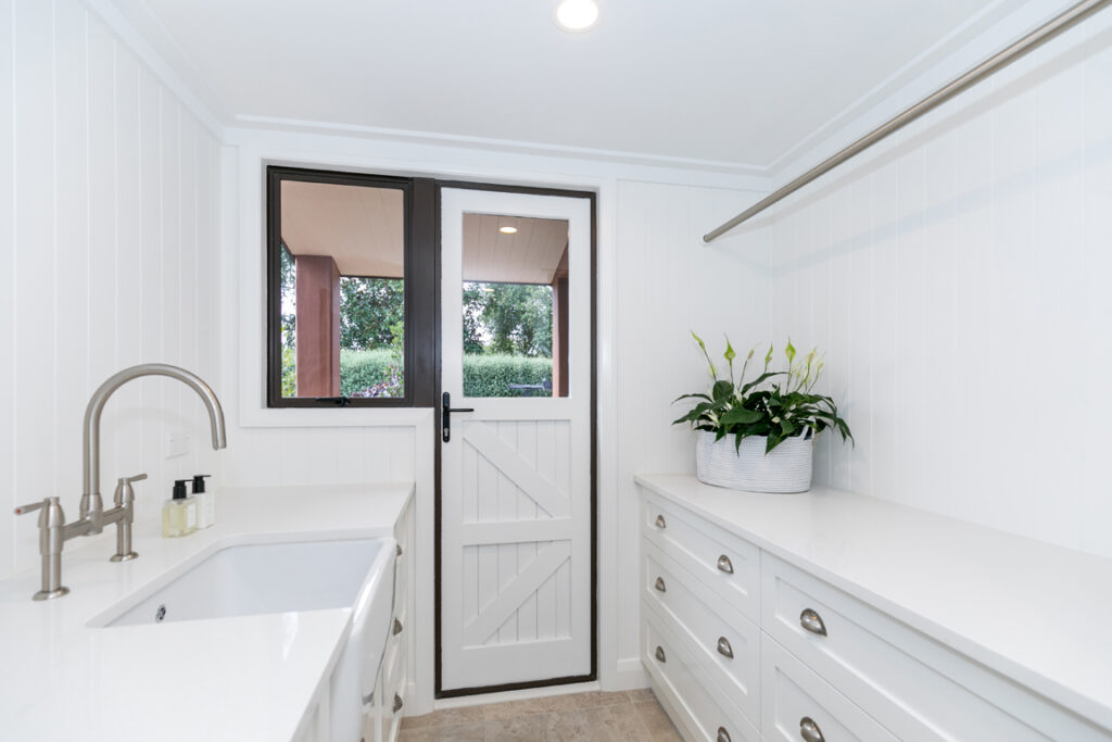 Renovated laundry with white cabinetry and butler sink