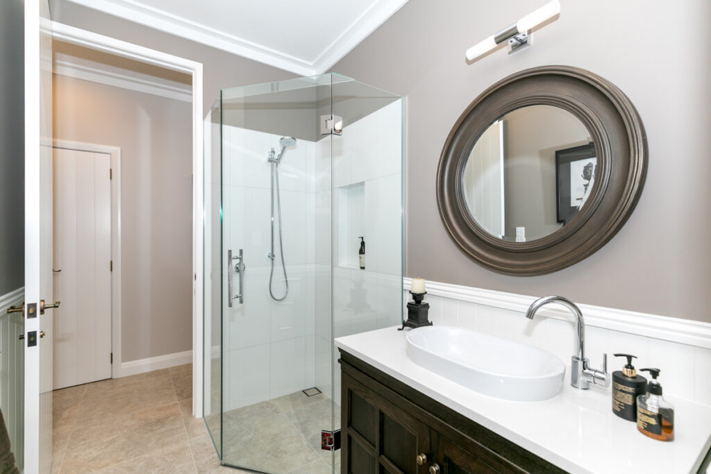 Luxury bathroom with shower, round mirror and dark vanity